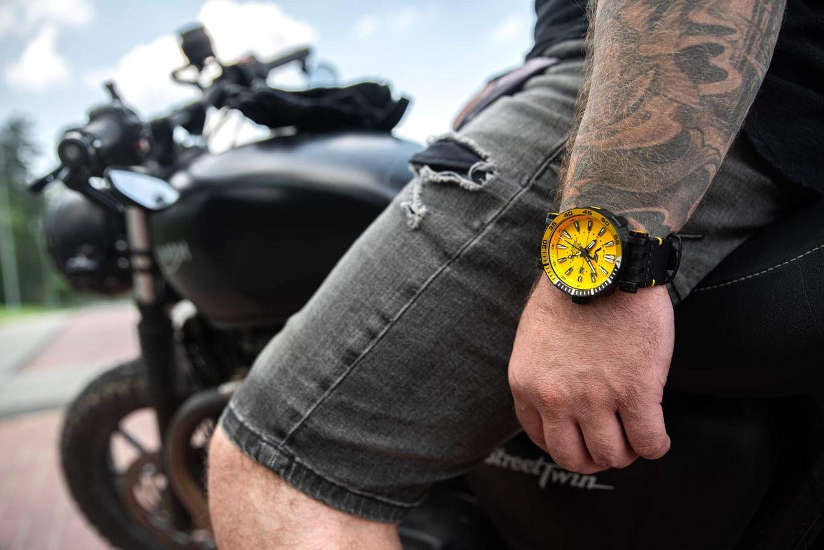 Man sitting on a motorcycle wearing a Vostok Europe watch with a yellow dial on a black strap