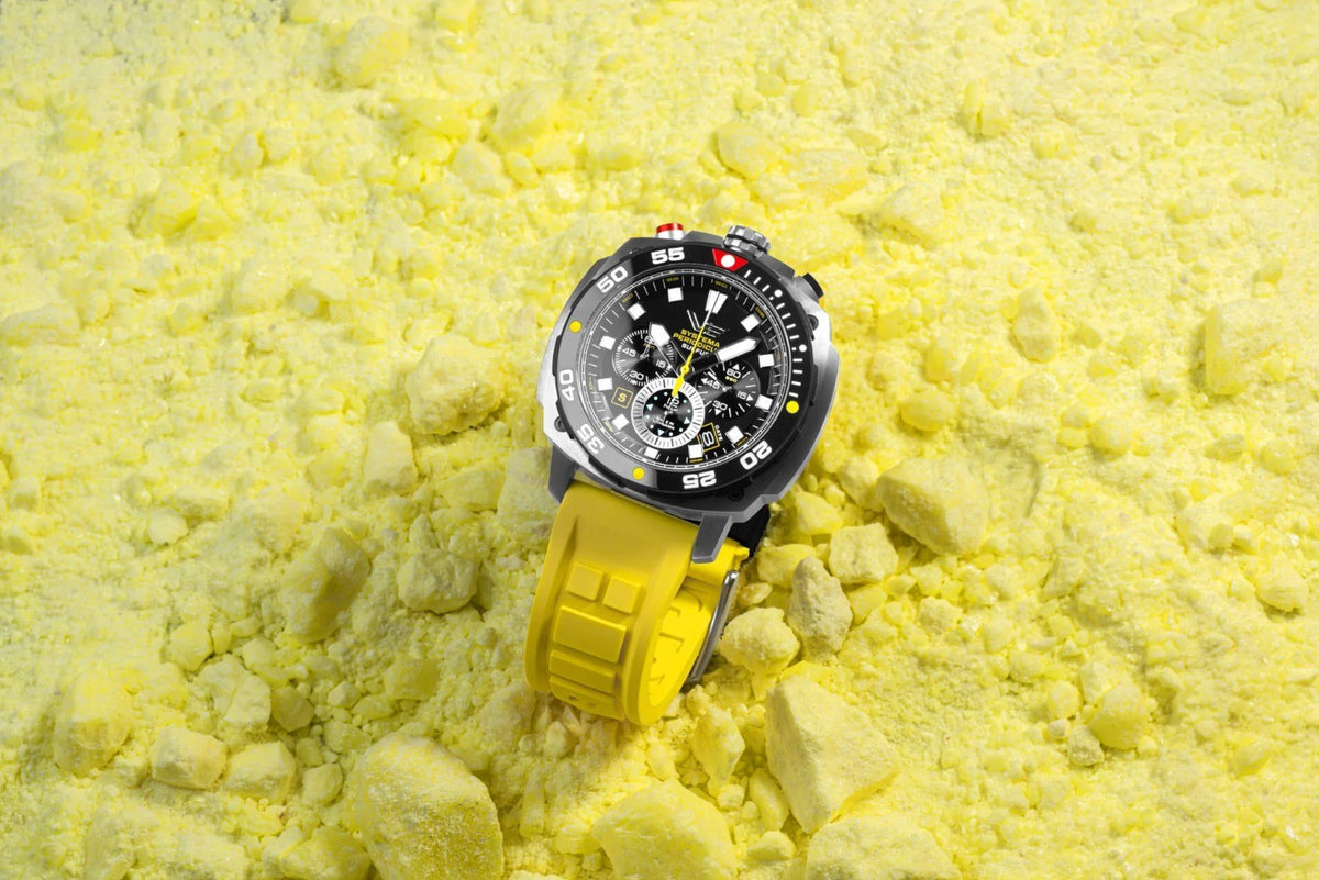 Black Systema Periodicum chronograph with yellow strap displayed on yellow mineral powder